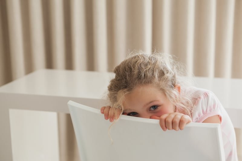 Little  girl hiding behind chair being shy and peeking over